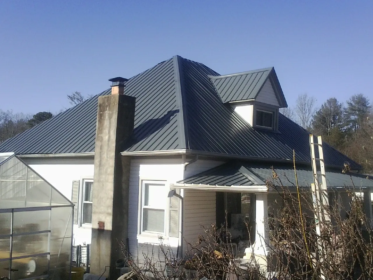 Dark blue standing seam metal roof on a white farmhouse with dormer — Slate & Tile Roof Repair by Roofing Brothers in Osage