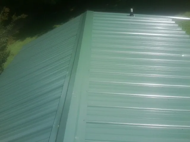 New green metal panels meeting at the ridge of a roof — Flat Roof Repair work by our crew in Osage