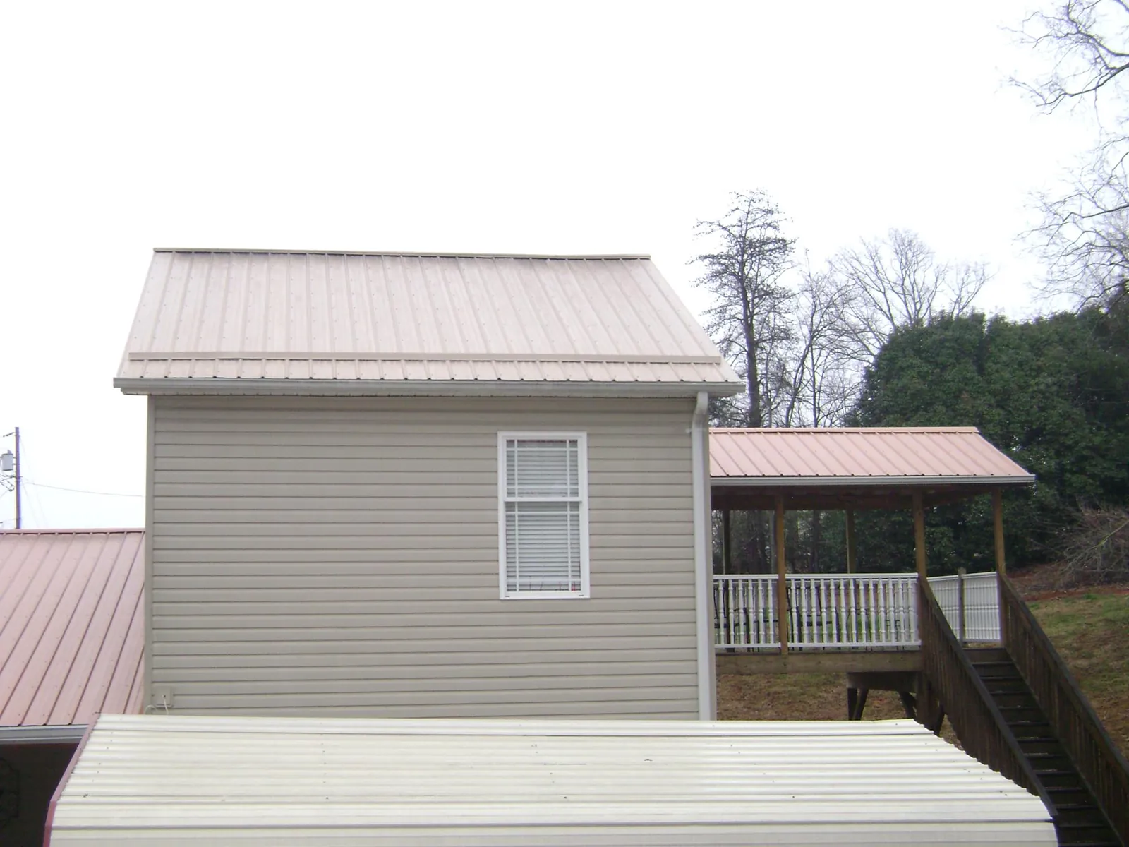 Tan metal roofs on a two story addition and attached porch, from a Roof Replacement job in Osage